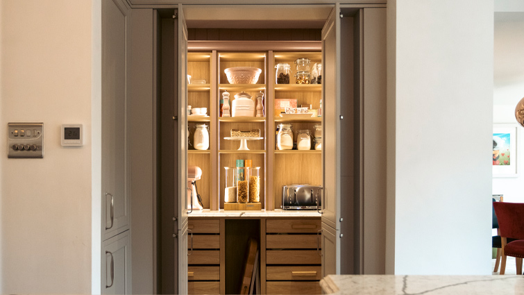 A grey walk-in pantry with internal lighting, crate drawers and light wood internals