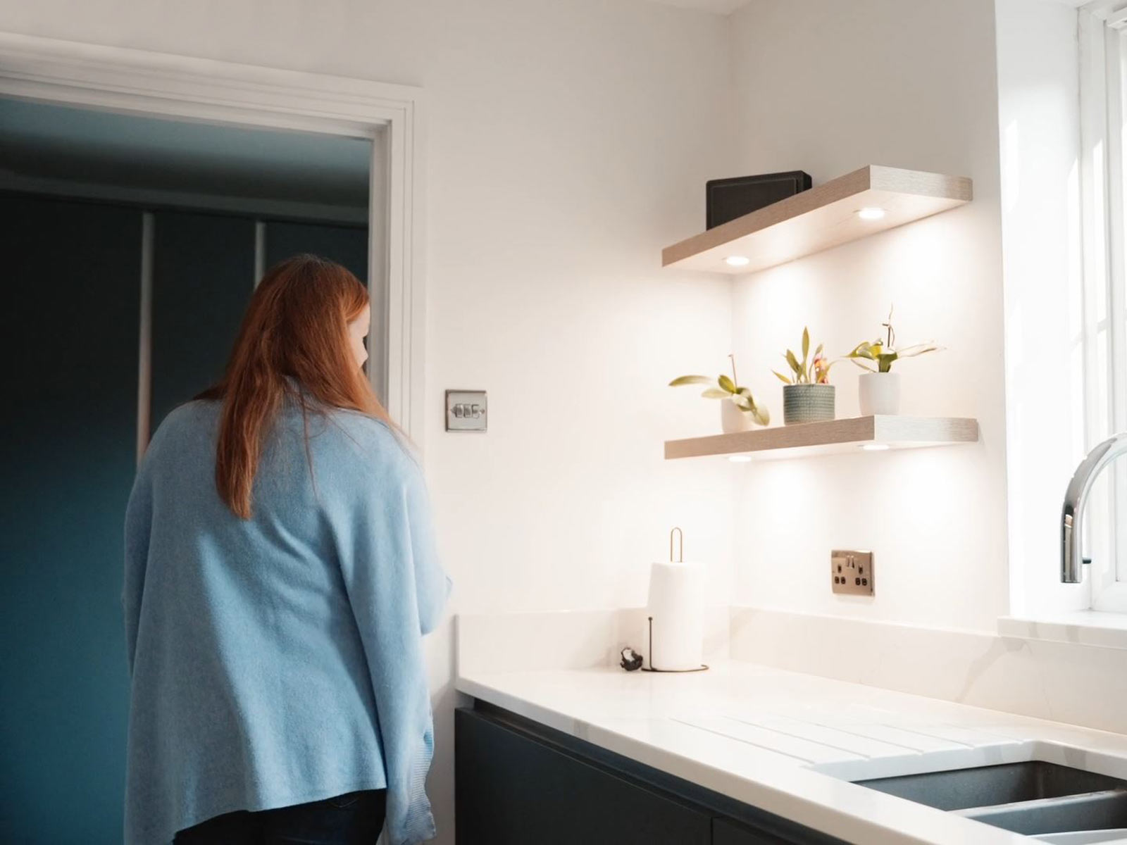 Lisa passing floating oak shelves with lighting to show off her utility room design