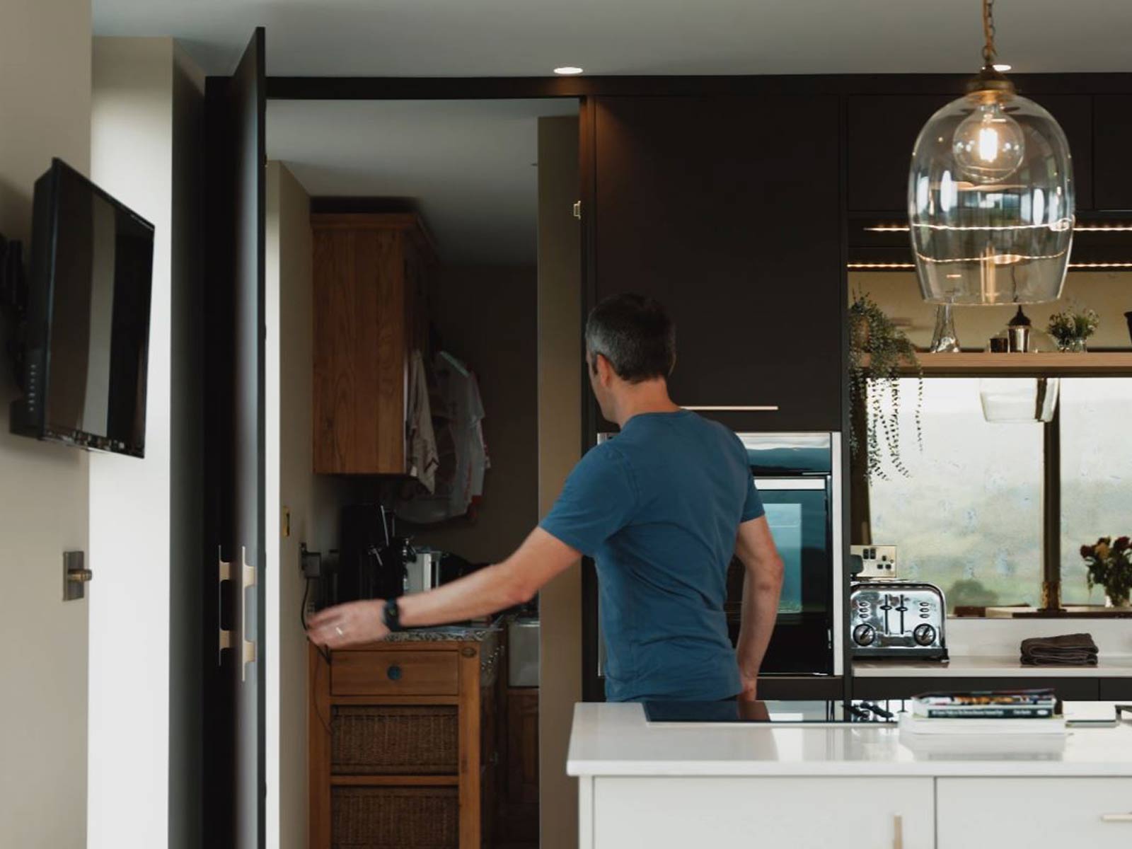 A man showing a secret room door built into his kitchen larder units